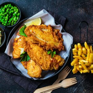 Fish and chips with green peas on dark background. British cuisine concept.