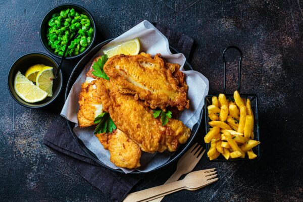 Fish and chips with green peas on dark background. British cuisine concept.